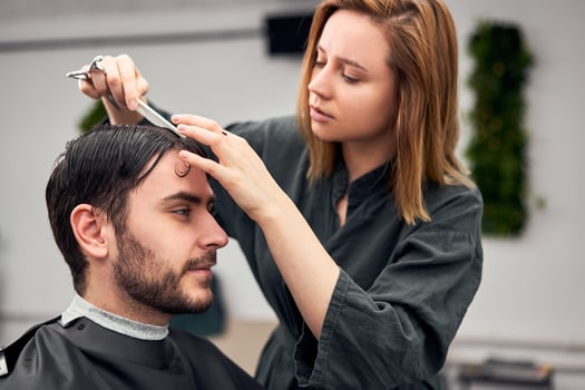 Handsome blue eyed man sitting in barber shop. Hairstylist Hairdresser Woman cutting his hair. Female barber. photo