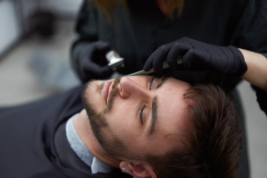 Young beautiful caucasian woman hairdresser cuts beard  handsome man at modern barbershop photo