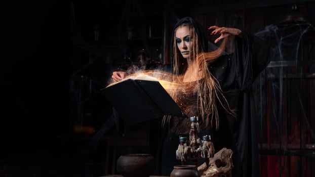 Halloween concept. Witch dressed black hood with dreadlocks standing dark dungeon room use magic book for conjuring magic spell photo