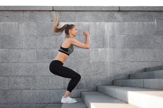 Urban sporty woman training. Female athlete doing squat jumps on urban stairs. photo