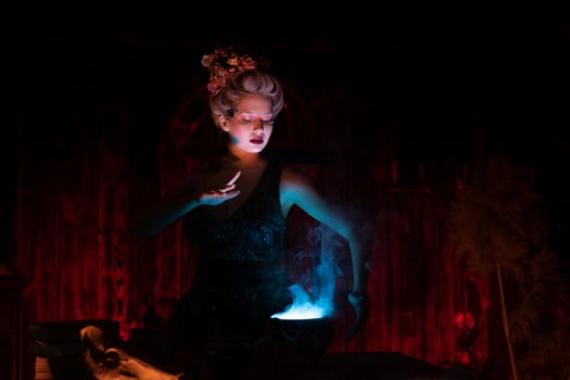 Halloween Witch with cauldron. Beautiful young woman conjuring, making witchcraft photo