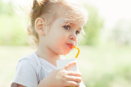 Sunny portrait of a little child drinking from a straw juiceon blurred summer background photo