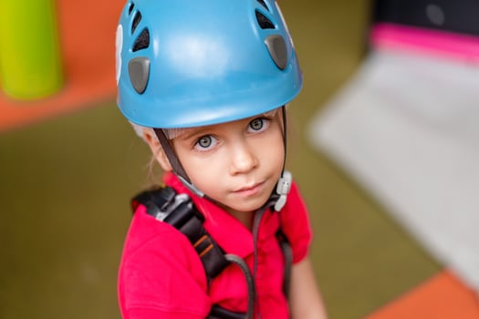 Cute little girl climber in blue protective helmet and gear for climbing standing in climber centre amusement park for children photo