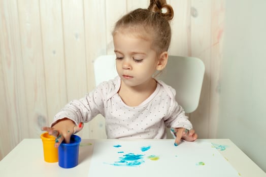 Beautiful little girl draws with finger paints on a white sheet of paper. Creative child development in kindergarten or free time at home photo