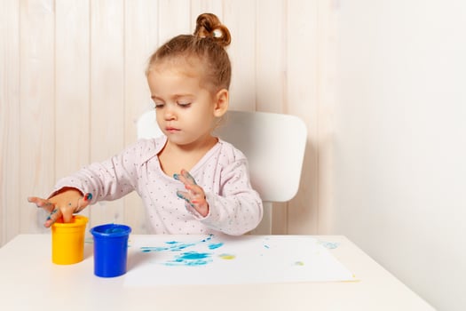 Beautiful little girl draws with finger paints on a white sheet of paper. Creative child development in kindergarten or free time at home photo