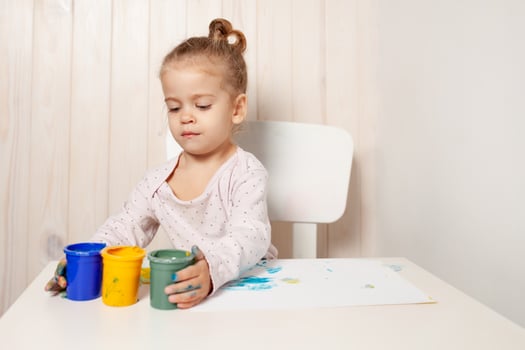 Beautiful little girl draws with finger paints on a white sheet of paper. Creative child development in kindergarten or free time at home photo