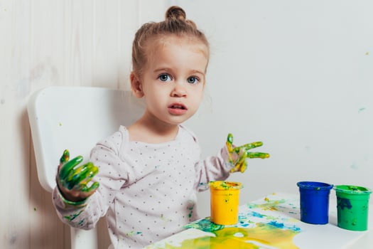 Beautiful little girl draws with finger paints on a white sheet of paper. Creative child development in kindergarten or free time at home photo