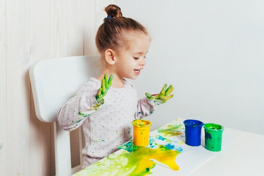 Beautiful little girl draws with finger paints on a white sheet of paper. Creative child development in kindergarten or free time at home photo