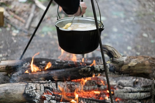 Camping outdoors. Cooking bowler hat hung on tripod over bonfire photo