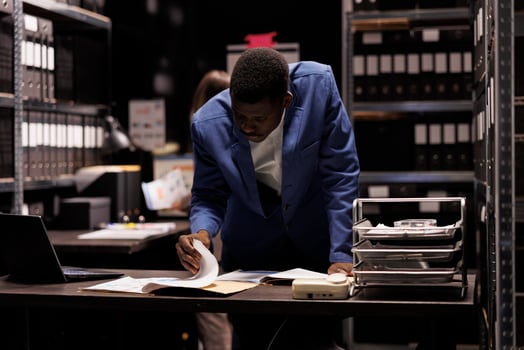 Depository worker reading administrative files, working late at night at management research in storage room. African american bookkeeper analyzing accountancy report in corporate repository photo