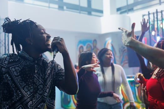 Smiling cheerful african american man singing in microphone while clubbing with friends. Young carefree clubber partying, holding mic and enjoying karaoke in crowded nightclub photo
