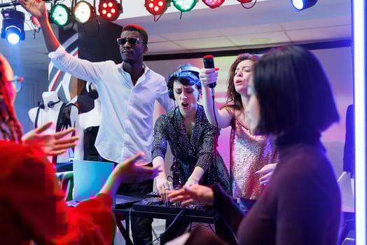 Electronic music band performing on stage in nightclub, while people partying on dancefloor. Woman dj using tracks mixer and singer giving mic to excited crowded to sing along photo