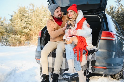 Smiling couple with dog sitting in open SUV car trunk in snowy forest. Enjoying each other in active winter holidays. photo