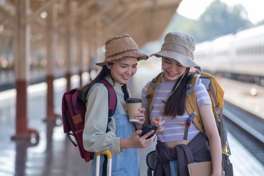 two young asian friends girls with backpacks at railway station waiting for train, Two beautiful women walking along platform at train station photo