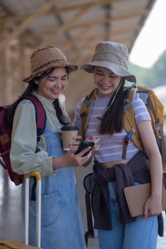 two young asian friends girls with backpacks at railway station waiting for train, Two beautiful women walking along platform at train station photo