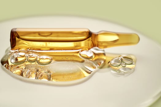 Ampoule in a drop of cosmetic gel on a green background. photo