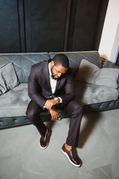 Young black man in suit on dark background sitting on a sofa. Fashion portrait of young man. photo