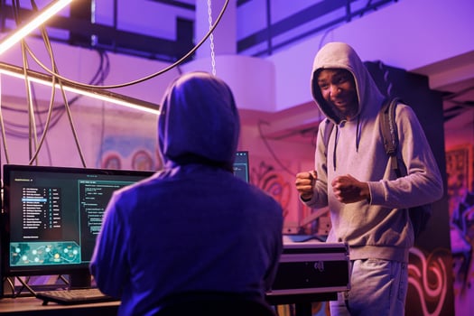 Cheerful internet scammers discussing phishing scam and planning online fraud. Smiling african american hacker explaining data breach idea to criminal in abandoned warehouse photo