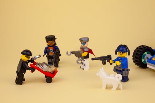 Ukraine, Kyiv - April 6, 2020 Lego robber with a gun takes away coins on a wheelbarrow. Lego man minifigure is carrying money on a trolley. Bank robbery game. Kids toys. Toy figurine man. photo