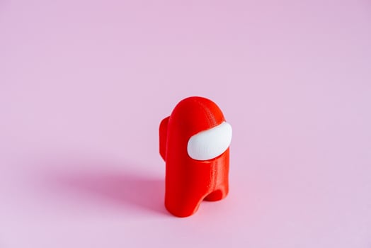 An unusual red figure of a man in a red spacesuit. Among us. The character of the popular game stands on a minimalist background. Computer games. amongas photo
