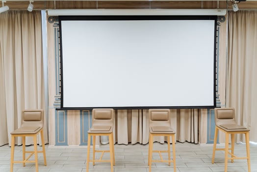 A white screen for showing the video hangs on the wall. Four chairs stand on the stage. Conference hall, business class for performances. photo