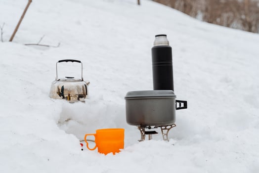 Cooking utensils for hiking, tea mug, hot drink thermos, pot on burner, kettle in the snow, winter tourism cold in the forest, breakfast in nature without people photo