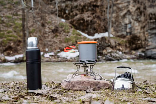 Tableware for camping on the background of the river, a place for outdoor recreation, camping equipment, thermos, kettle, pot, gas burner, camping gas. photo
