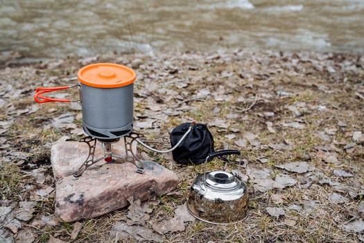 Tourist utensils, silver kettle, aluminum pot with handles and lid, gas camping burner, field kitchen, cook food in the forest. photo