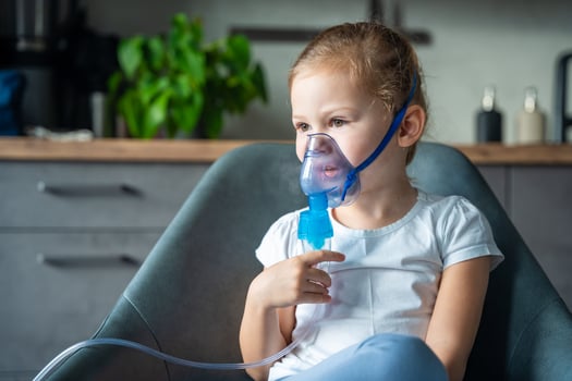 Cute little girl are sitting and holding a nebulizer mask leaning against the face at home on sick leave, airway treatment concept photo