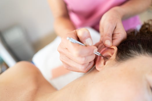 Crop masseuse applying flexible massage ear pen during auriculotherapy tr in salon photo