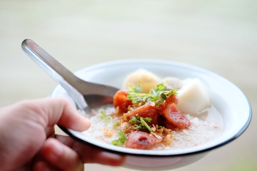 Woman hand holding rice porridge with pork and Fried Chinese sausage in white bowl.  Favorite food and tradition breakfast in Thailand photo