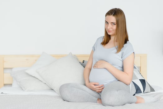 Pregnant young European woman sitting on a large bed and stroking her big belly, 7 month pregnancy, waiting for the birth of her baby. photo
