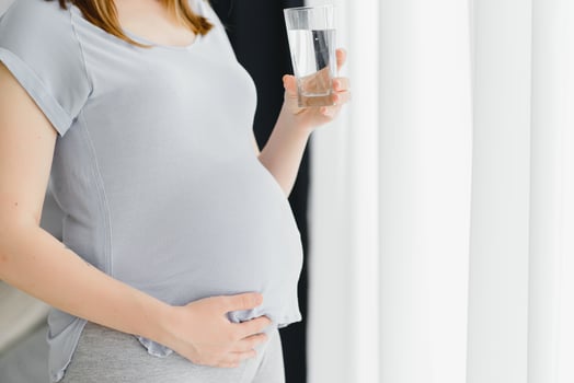 Young pregnant woman standing and drinking water while relax at home. photo