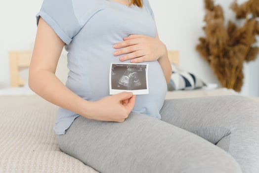 Pregnant woman is holding her stomach and a photo of her Ultrasound