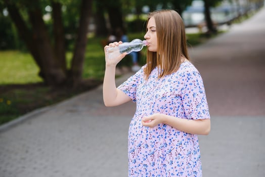 Pregnant woman stands in the park with a bottle of water. copy space photo