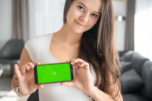 Young smiling woman shows smartphone with green screen in home living room closeup. Technology, gadget, connection. Advertising area, workspace mock up. High quality photo