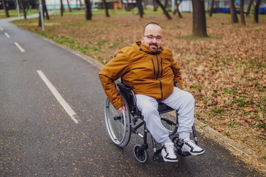 Portrait of happy paraplegic handicapped man in wheelchair in park. He is rolling on pathway. photo