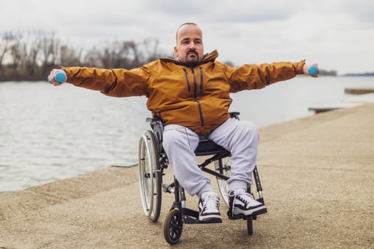 Paraplegic handicapped man in wheelchair by the lake. He is exercising with weights. photo
