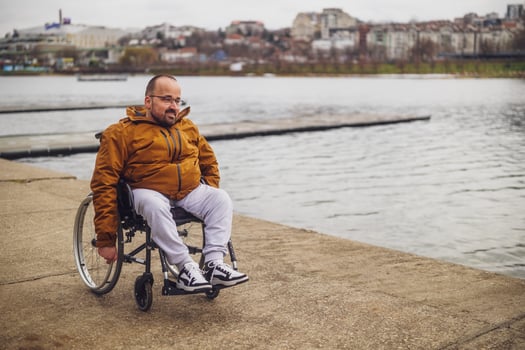 Happy paraplegic handicapped man in wheelchair by the lake. He is rolling on walkway. photo