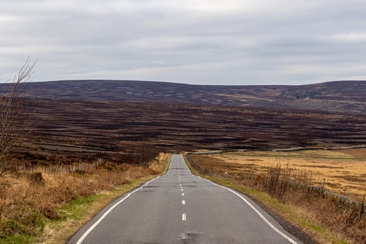 Empty rural road leading through a barren landscape with overcast skies in Peak District, England. photo