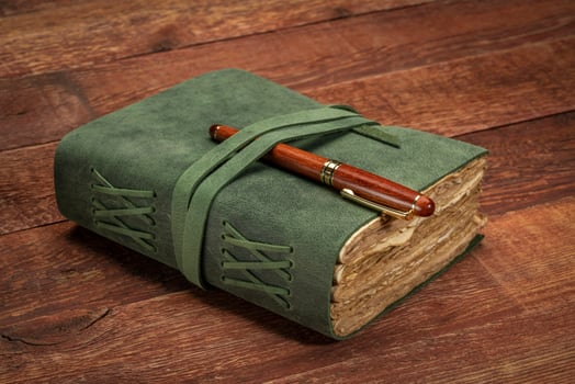 retro leather-bound journal with decked edge handmade paper pages with a stylish pen on a rustic barn wood table, journaling concept photo