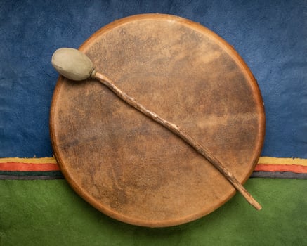 handmade, native American style, shaman frame drum covered by goat skin with a beater against colorful abstract paper landscape photo