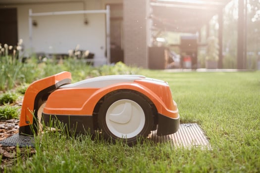 An orange robotic lawn mower stands on the base and is charged from electricity in the courtyard photo