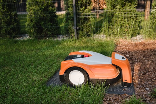 An orange robotic lawn mower stands on the base and is charged from electricity in the courtyard photo