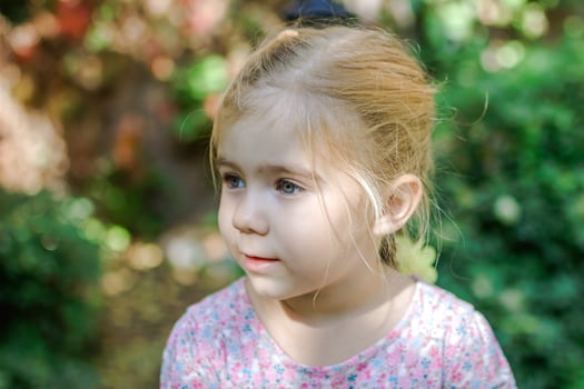 Adorable Little Girl with Blonde Hair Looking Away in Beautiful Garden Setting photo