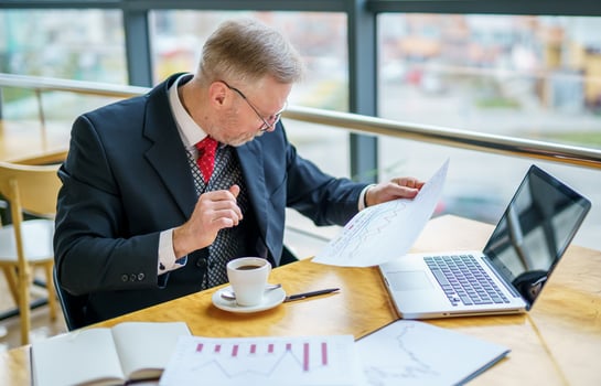Elderly businessman using laptop and taking notes working while sitting in modern office. Selective Focus photo