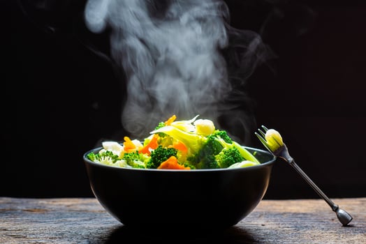 The steam from the vegetables carrot broccoli cauliflower on black bowl, A bowl of hot food on wood table on black background photo