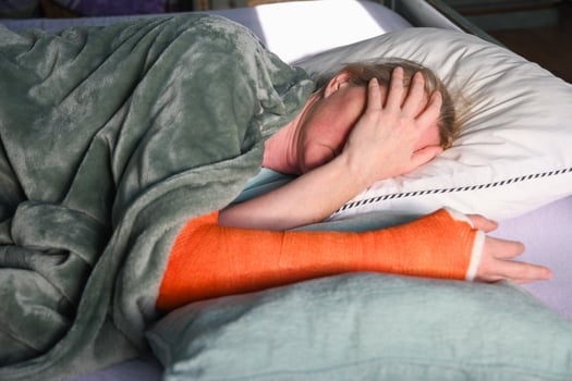 woman with a broken right arm with an orange fiberglass plaster cast sleeps in bed with a pillow under the cast photo