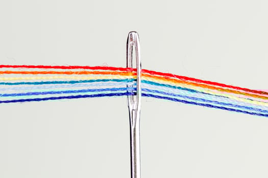 multi-colored threads for sewing in the form of a rainbow pass through an antique needle on a white background photo