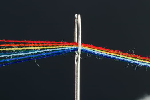 multi-colored threads for sewing in the form of a rainbow pass through an antique needle on a black background photo